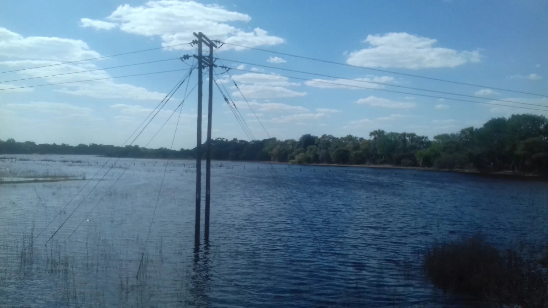 Power lines above a broad blue stretch of the Thamalakane at Maun